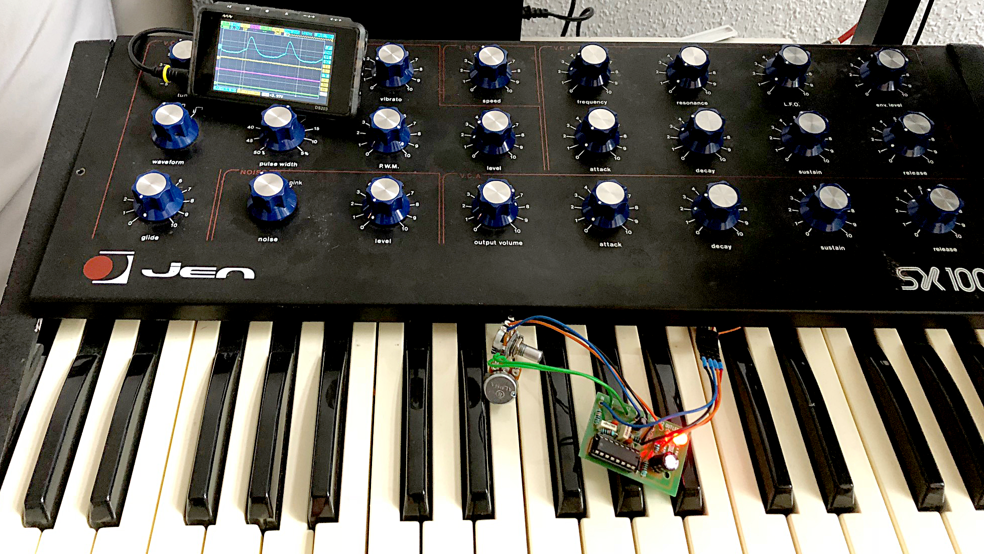 JEN synth, with osc screen displaying a distorted sawtooth wave, and the overdrive circuit lying naked on the keyboard